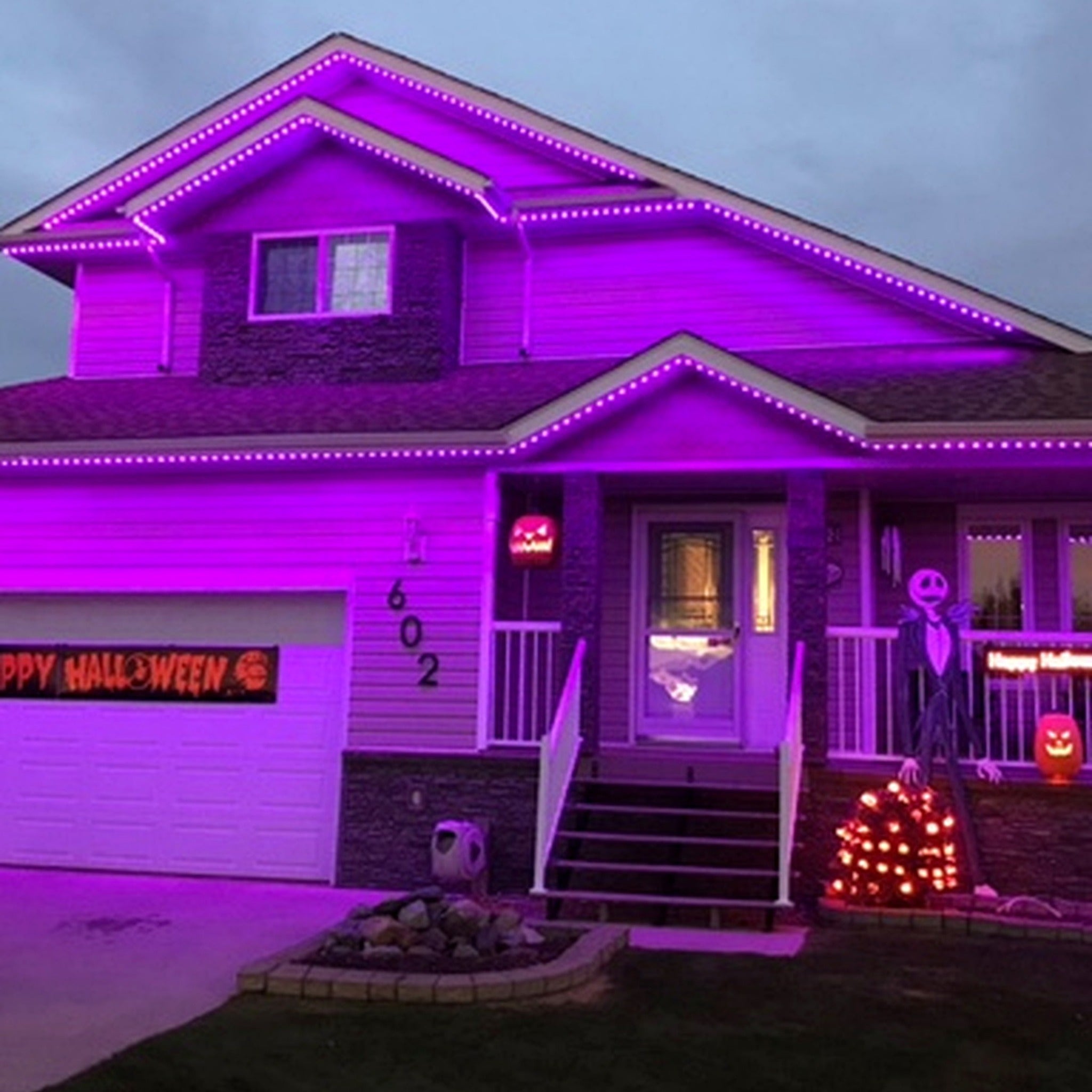 Home decorated for Halloween with purple permanent LED roofline lighting and pumpkin decor