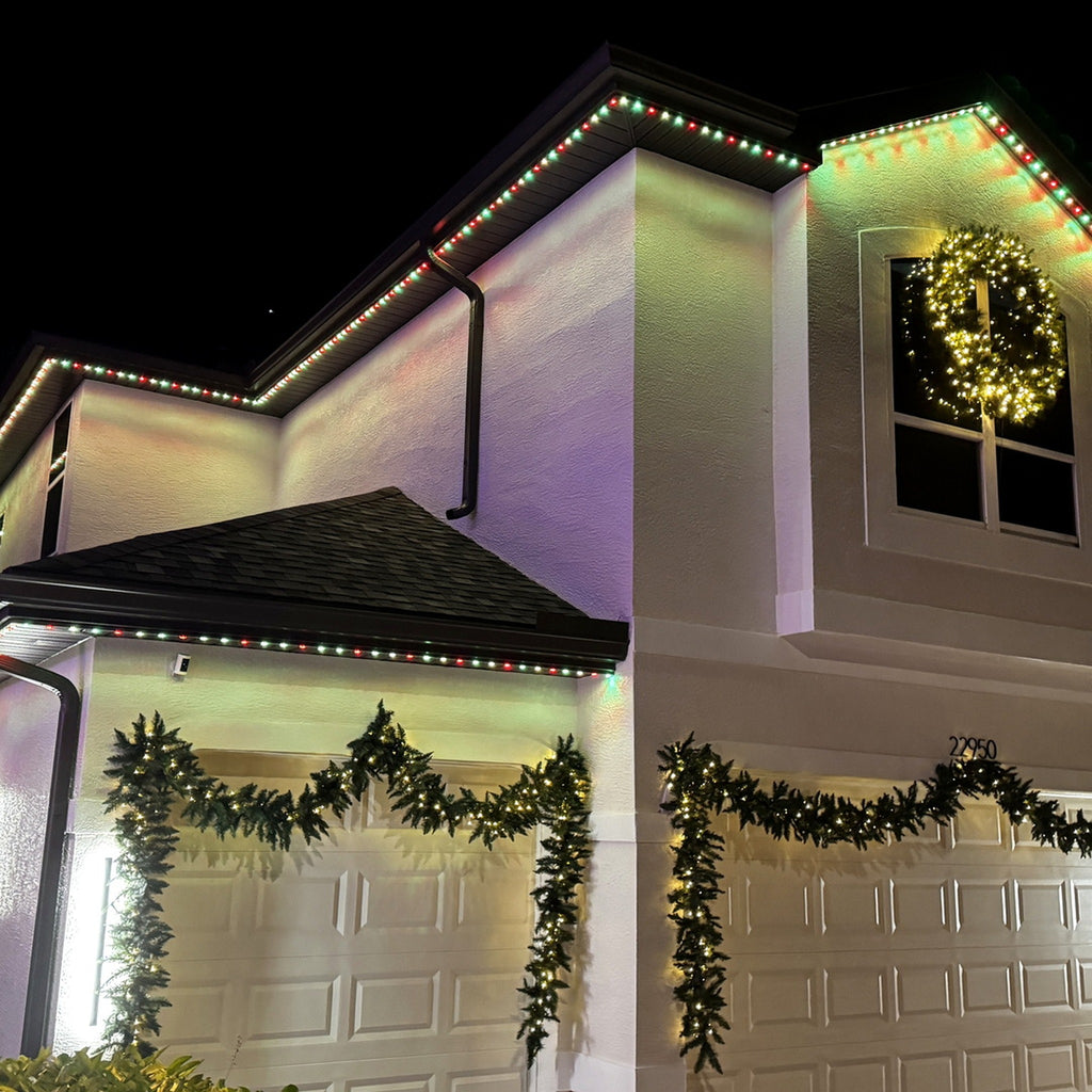 Home with red and green permanent LED roofline lighting and Christmas garland over the garage