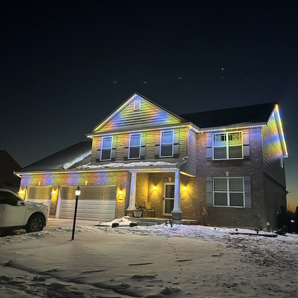 Snow-covered two-story home with multicolor rainbow permanent LED roofline lighting