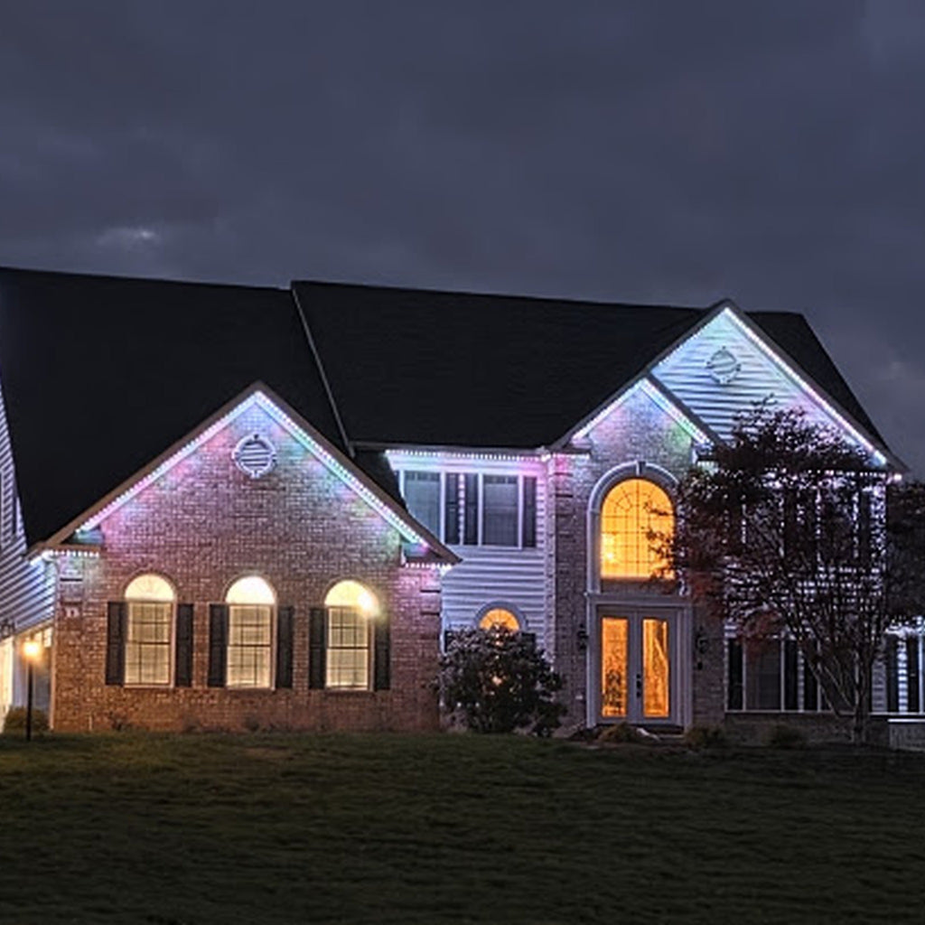Two-story brick and siding estate home with white and multicolor permanent LED lights along the gables