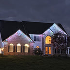 Two-story brick and siding estate home with white and multicolor permanent LED lights along the gables