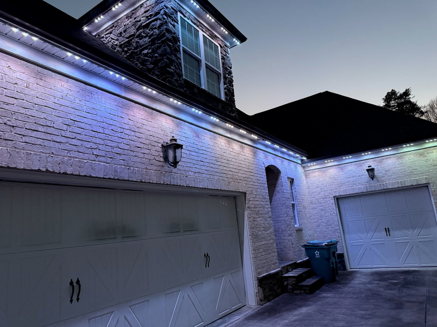 Cool-white permanent LED roofline lights installed above a brick home garage