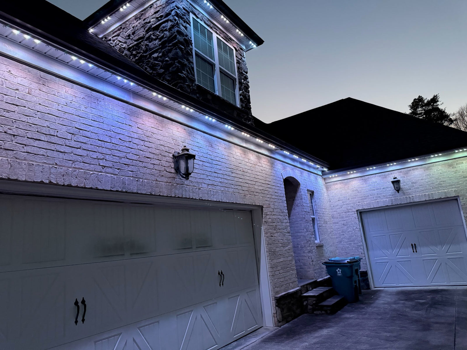 Cool-white permanent LED roofline lights installed above a brick home garage